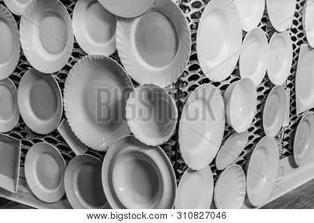 Black And White Photography Of White Crockery Plates And Dishes Are Displayed On White Lattice Wall.