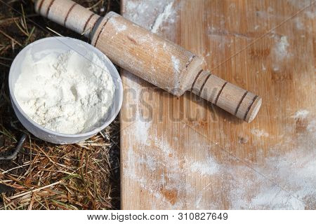 Top View Of The Working Board With Flour And Rolling Pin Next To A Bowl Of Flour That Lies On The Gr