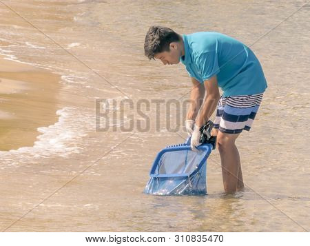 Cyprus, Karavas, Alsancak - June 10, 2019: Young Worker Cleaning The Coast From Debris And Waste. Ma