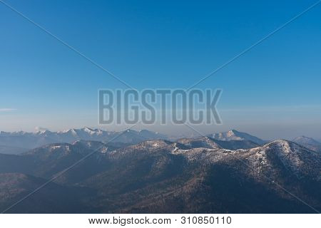 Panoramic View Of Beautiful Mountain Landscape, Snowy Mountain Peaks Covered By Forest With A Dark B
