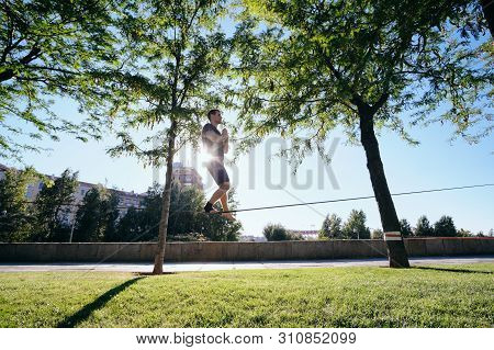 Man Training With Trickline Slackline In City Park