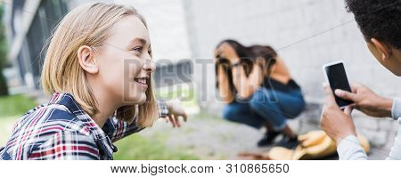 Panoramic Shot Of African American Boy And Blonde Teenager Pointing With Finger And Shooting Scared 