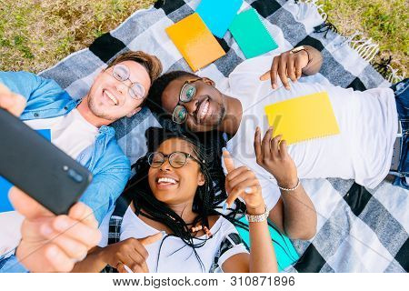 Top View Of A Happy African Male, Gemale Teenagers And Their Caucasian Boy Friend Lying On A Grass W