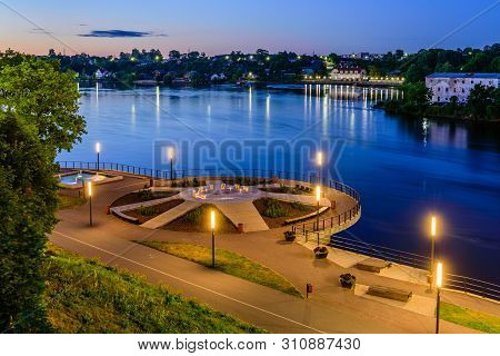 Sightseeing Of Estonia. Beautiful Night View Of Narva. River Promenade And The Square Of The Sun Wit