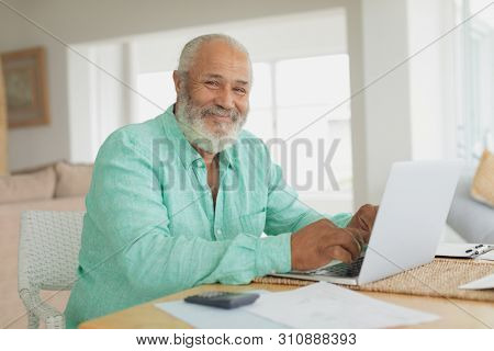 Side view of African-American smiling man using laptop on table indoor. Authentic Senior Retired Life Concept