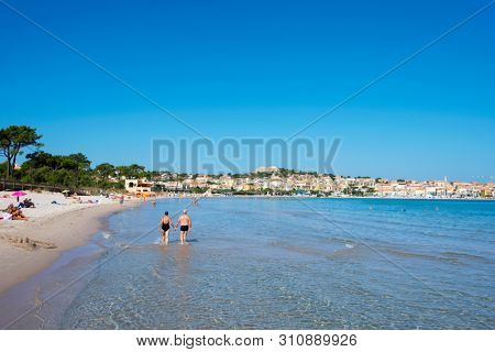 CALVI, FRANCE - SEPTEMBER 21, 2018: People walking by the seashore and swimming in the Medtierranean sea at the Plage de Calvi beach, the main beach of Calvi, in Corsica, France