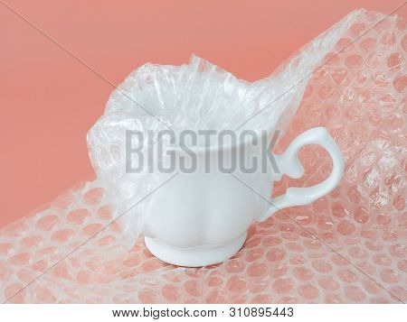 White Elegant Tea Cup Half Packaged With White Transparent Bubble Wrap On A Pink Background. Materia