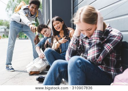 Pretty And Smiling Friends Bulling And Pointing With Fingers At Sad Blonde Teen