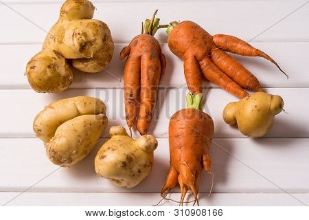 Flat Lay Some Ugly Curved Ogranic Carrots And Potatoes On White Wooden Background.
