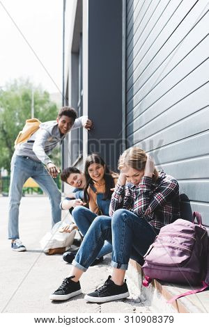 Pretty And Smiling Friends Bulling And Pointing With Fingers At Sad Blonde Teen