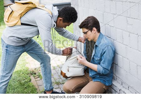 African American Boy Taking Backpack From Frightened Boy In Glasses