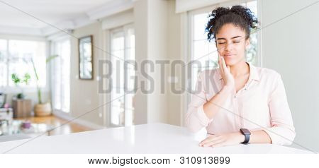 Wide angle of beautiful african american woman with afro hair touching mouth with hand with painful expression because of toothache or dental illness on teeth. Dentist concept.
