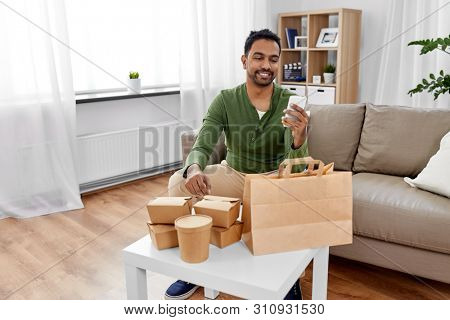 communication, leisure and people concept - indian man using smartphone for takeaway food order check up at home