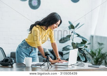 Pretty Radio Host Using Laptop While Standing At Wokplace In Studio
