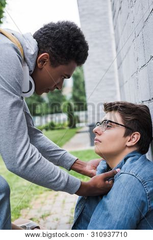 Aggressive And Brunette African American Boy Bulling Frightened Boy In Glasses