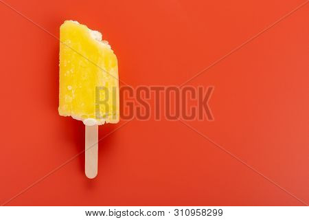 Yellow Popsicle With A Couple Of Bites On An Orange Background