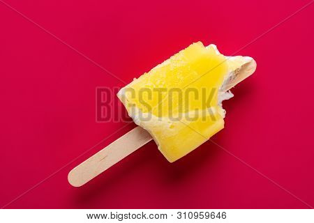Yellow Popsicle With A Couple Of Bites On A Red Background