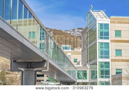 Skybridge Connected To A Modern Building With Mountain And Blue Sky Background