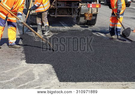 The Working Team Smoothes Hot Asphalt With Shovels By Hand When Repairing The Road.