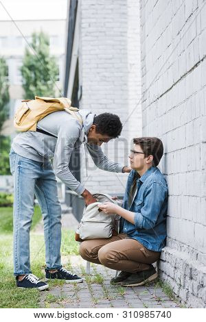 African American Boy Taking Backpack From Frightened Boy In Glasses