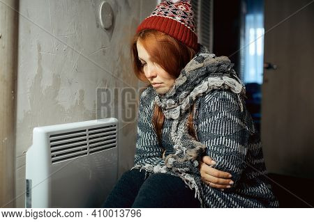 A Woman Is Warming Herself At The Radiator In A Cold House, Problems With Heating, Heating The Room 