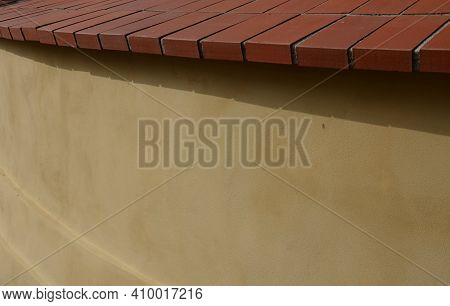 Crown Wall, Garden Fence. Fired Bricks Protect The Low Thick Plastered Wall Of Yellow Color. Wall In