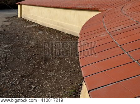 Crown Wall, Garden Fence. Fired Bricks Protect The Low Thick Plastered Wall Of Yellow Color. Wall In