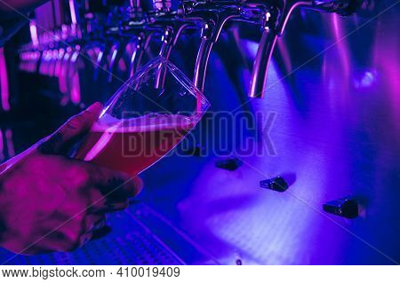 Close-up Beer Glass In Barman Hand In Multicilored Neon Light.