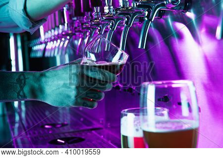 Close-up Beer Glass In Barman Hand In Multicilored Neon Light.