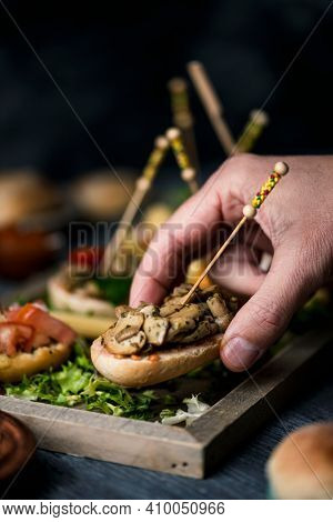 closeup of a young man taking a vegan spanish pincho from a tray with some other pinchos made with bread with different toppings
