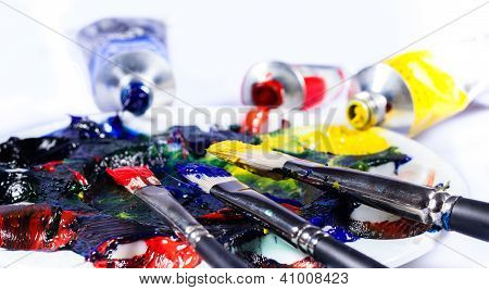 Ver os uma paleta de cores com pincéis e tubos de tinta