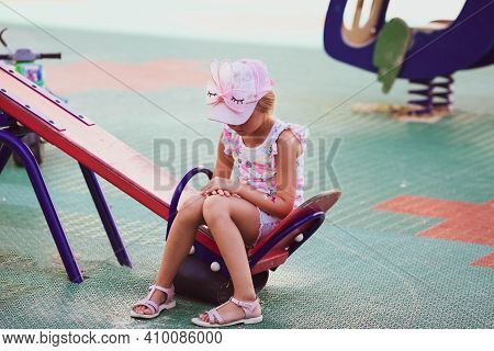 Sad Girl Sits Alone On A Swing In The Playground. Outcast, Loneliness.