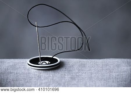 The Black And White Button Is Sewn With A Sewing Needle And Black Thread To Hold The Two Fabrics Tog