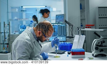 Scientist In Medical Laboratory Examining Drug Discovery Putting Blood Sample In Petri Dish With Mic