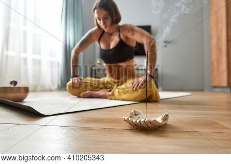 Healthy Young Woman Doing Uddiyana Bandha Abdominal Lock While Sitting On Floor Mat Beside Burning S