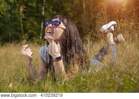 Happy Beautiful Young Woman In Sunglasses Smiles And Lies On A Meadow In The Grass In The Sunshine E