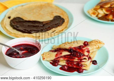 Blini Pancakes With Red Berry Jam Close-up On A Blue Plate On A Light Background . Traditional Russi