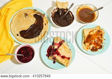 Blini Pancakes With Chocolate, Caramel And Jam Top View Close-up On A Blue Plate On A Light Backgrou