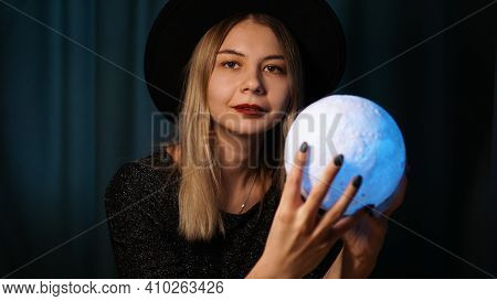 A Young Woman Fortune Teller In A Hat Is Holding A Magic Ball. Beautiful Psychic Woman Is Guessing W