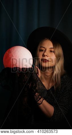 A Young Woman Fortune Teller In A Hat Is Holding A Magic Ball. Beautiful Psychic Woman Is Guessing W