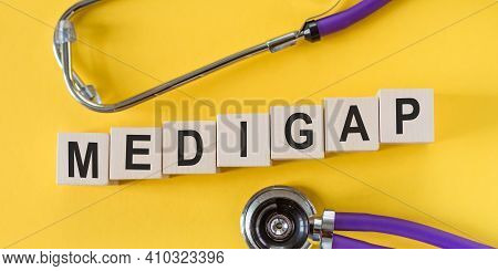 Word Medigap Building From Wooden Cubes On Yellow Desk With Stethoscope.