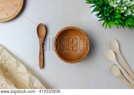 Wooden Utensils On The Kitchen Table. Round Wooden Plates, A Wooden Spoons, A Green Plant. The Conce