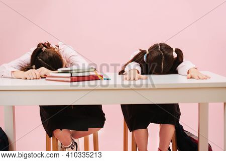 Happy Little Twin Schoolgirls Sleeping On A Schooldesk Face Down. Over Pink