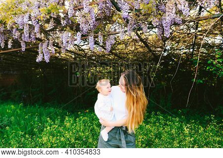 Woman Is Holding Her Toddler Under A Wysteria Tree