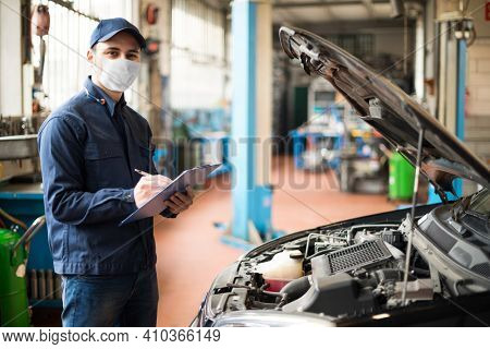 Masked car mechanic repairing a car, covid coronavirus work concept