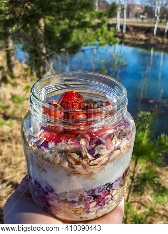Hand Holding Healthy Breakfast Overnight Oats With Fresh Strawberries, Blueberries In A Glass Jar Wi