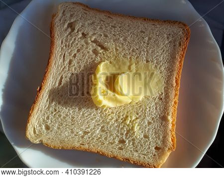 Slice Of Toast Bread With A Piece Of Butter On A White Plate In A Sunlight