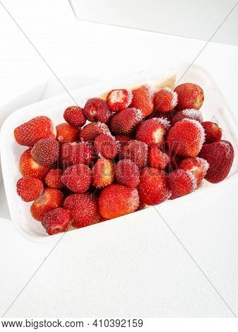 Close Up Of Frozen Strawberries With Frost On Them In A Plastic Container On White Background