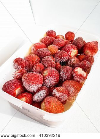 Close Up Of Frozen Strawberries With Frost On Them In A Plastic Container On White Background