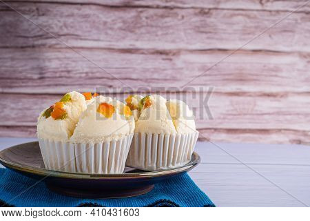 Side View Of Thai Steamed Cupcakes Topped With Dry Fruit On A Plate Placed On A Blue Cloth With Wood
